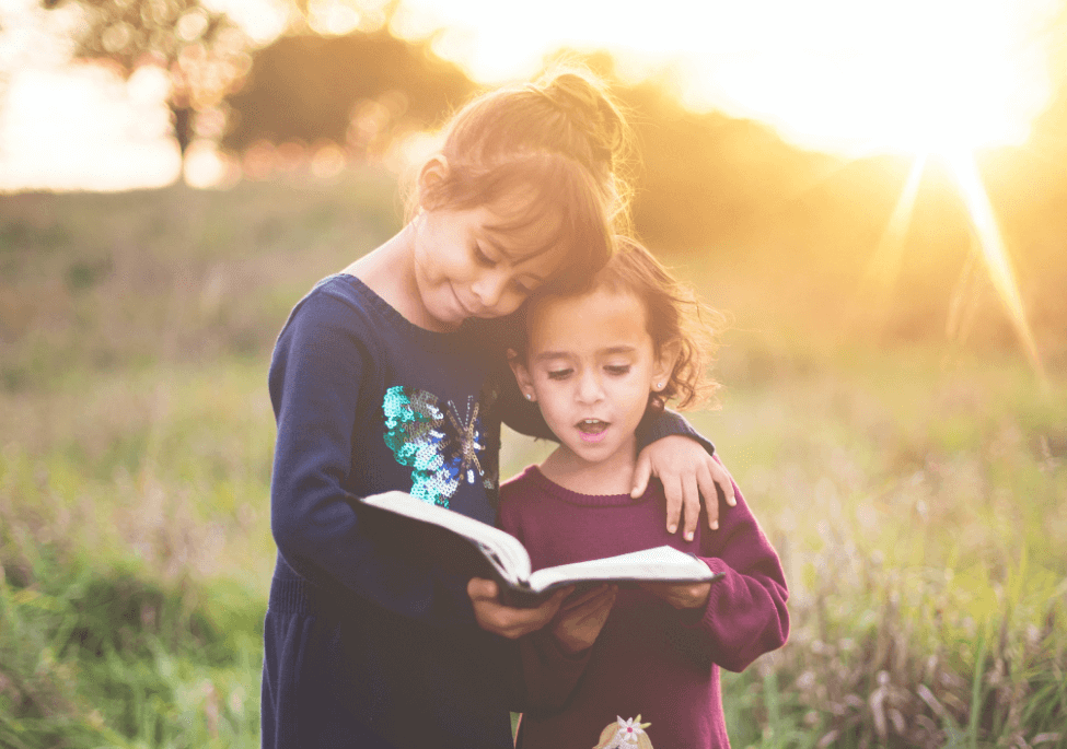 Two young female children singing from a hymn book during a church ministry